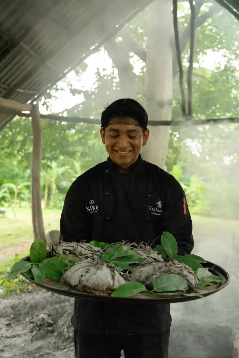 Cocinero de Cenote San Ignacio con una charola de alimentos envueltos en hoja de plátano